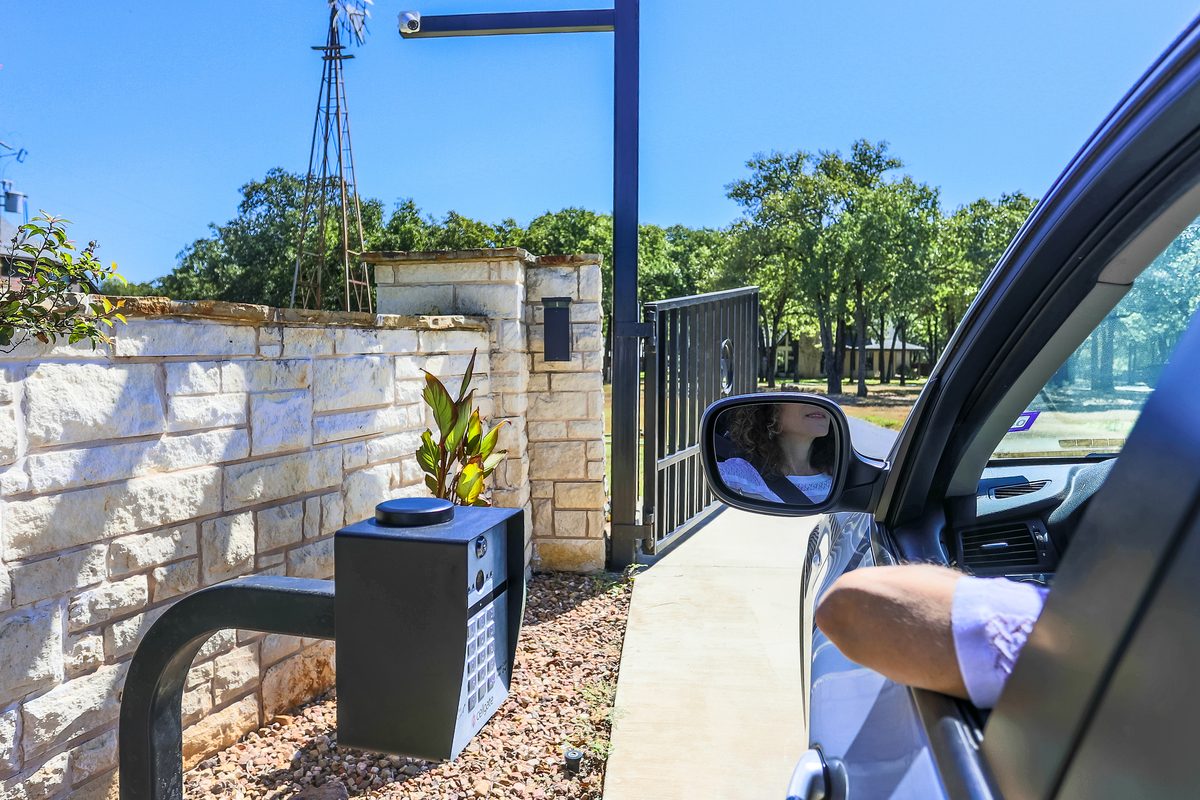 Car pulling up to a CellGate Watchman W410 with a pole-mounted external camera covering the gated driveway entrance